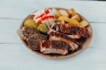 Delicious beef ribs with sauce, fried potatoes, cucumber, cabbage and khlobe in a paper plate on a wooden table. takeaway street food