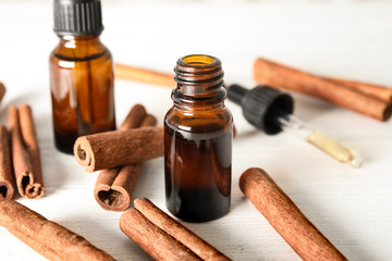 Bottles of essential oils and cinnamon sticks on white wooden table