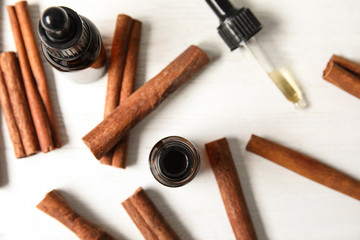 Bottles of essential oils and cinnamon sticks on white wooden table, flat lay