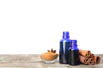 Fototapeta na wymiar Bottles of essential oils, cinnamon sticks and powder on wooden table against white background. Space for text