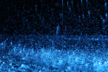 Heavy rain falling down on ground against dark background, toned in blue
