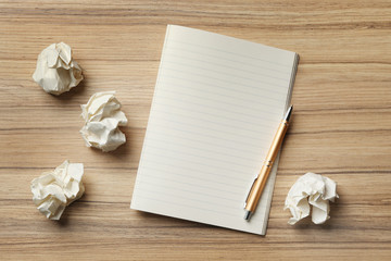 Fototapeta premium Empty notebook with pen and crumpled paper balls on wooden table, flat lay. Space for text