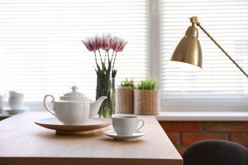Tea set on table near window with blinds indoors