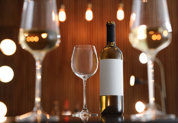 Bottle of wine and empty glass on table against blurred background. Space for text