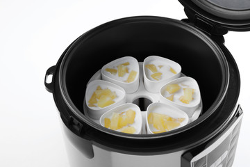 Cups of pineapple yogurt in multi cooker on white background, closeup