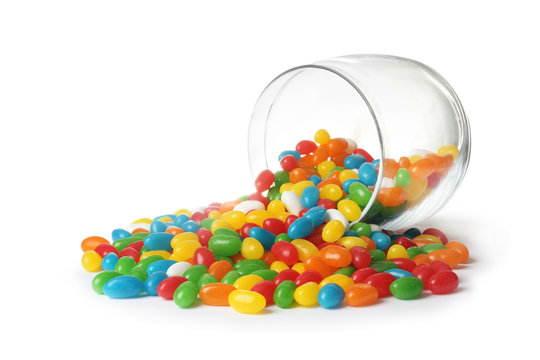 Glass jar and scattered bright jelly beans isolated on white