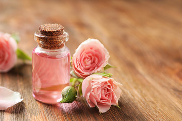 Fototapeta na wymiar Bottle of rose essential oil and flowers on wooden table, space for text