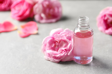 Bottle of rose essential oil and fresh flowers on table, space for text