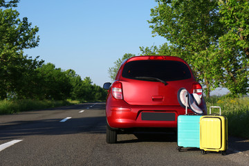 Color suitcases with hat near family car on highway. Space for text