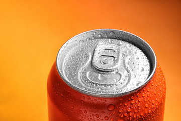 Aluminum can of beverage covered with water drops on orange background, closeup. Space for text