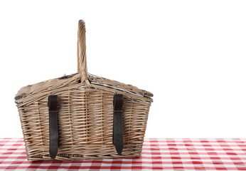 Closed wicker picnic basket on checkered tablecloth against white background