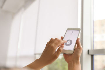 Woman using smart home application on phone to control window blinds indoors, closeup. Space for text