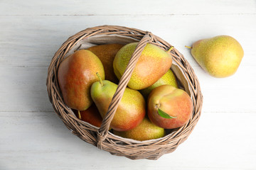Ripe juicy pears in wicker basket on white wooden table, above view
