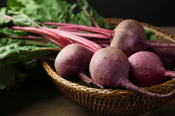Wicker basket with bunch of fresh beets on table, closeup