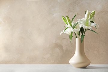 Vase with beautiful lilies on table against light brown background, space for text