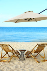 Empty wooden sunbeds and beach accessories on sandy shore