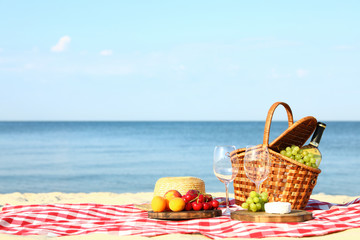 Checkered blanket with picnic basket and products on sunny beach. Space for text