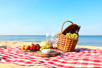 Checkered blanket with picnic basket and products on sunny beach