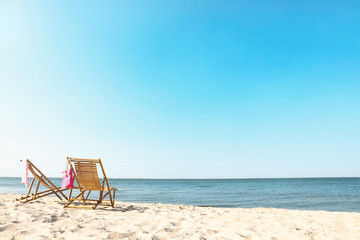 Empty wooden sunbeds and beach accessories on sandy shore