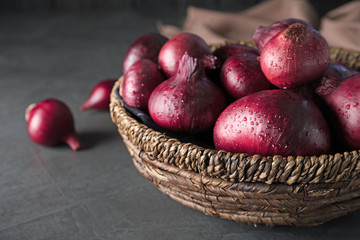 Wicker bowl of wet whole red onion bulbs on grey table, closeup