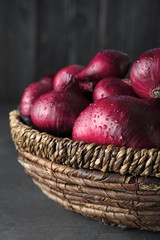 Wicker bowl of wet whole red onion bulbs on grey table, closeup