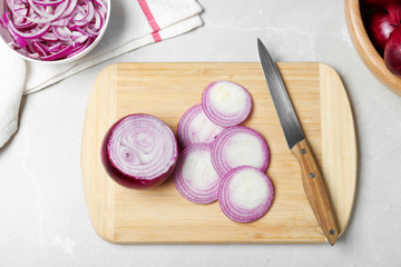 Wooden board with cut fresh red onion and knife on marble table, flat lay