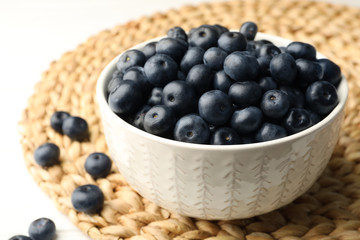 Bowl of fresh acai berries on wicker mat, closeup view. Space for text