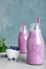 Glass bottles of blueberry smoothie and bowl with fresh berries on grey marble table