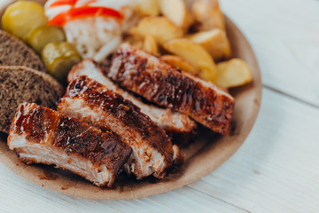 Delicious beef ribs with sauce, fried potatoes, cucumber, cabbage and khlobe in a paper plate on a wooden table. takeaway street food