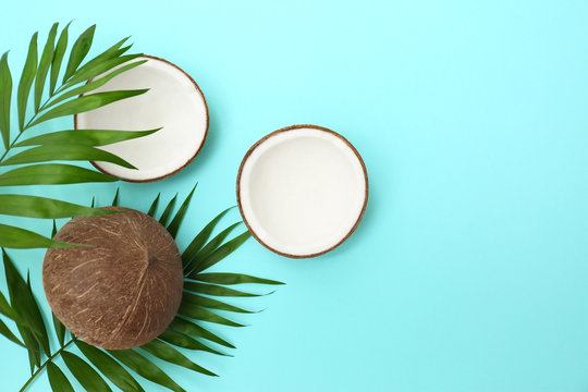 Fresh coconuts and palm leaves on light blue background, flat lay. Space for text