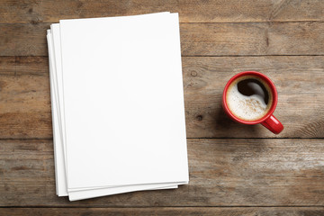Blank paper sheets for brochure and cup of coffee on wooden background, flat lay. Mock up