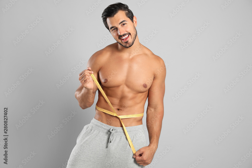 Sticker Young man with slim body using measuring tape on grey background