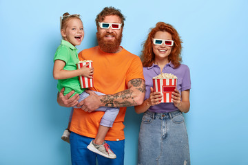 Optimistic three family members laugh happily, watch comedy in cinema together, enjoy eating delicious popcorn, express positive emotions, laugh at funny scene. Leisure, parenthood, children