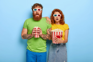 Frightened red haired woman and man being deeply impressed by film, forget they are in cinema,...