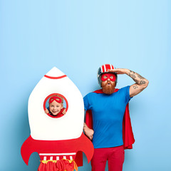 Super father wears mask, blue t shirt and red cloak, looks surprisingly into distance, plays with...