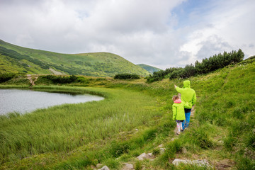 Obraz premium Dad and daughter walk around the mountain lake. Dad shows a cloudy sky.