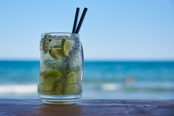 A steamed glass of Mojito on the bar with two black tubes.Against the sea and blue sky.