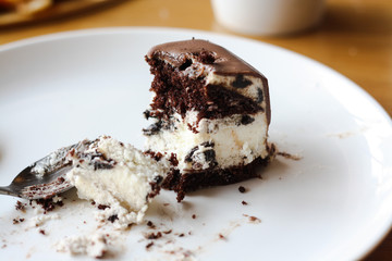 Half-eaten chocolate cream cake on a white plate, spoon