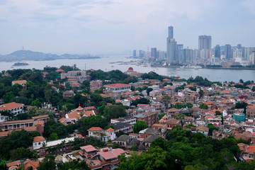 Fototapeta na wymiar aerial view of Gulangyu(Kulangsu) Island. Dense red retro houses and trees. Modern skyscrapers on the other side of the river. Famous tourist city of China