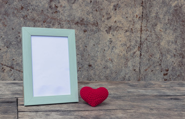 Photo frame with red heart on the retro wooden table with stone wall background