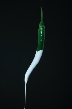 Dripping white paint of fresh green pepper on a black background. Creative poster.