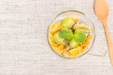 Delicious and healthy yogurt parfait made with homemade yogurt, kiwi fruit, corn flakes and sweet basil seeds with wooden spoon on wooden background; healthy dietary start eating good food.