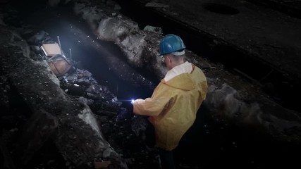 Dangerous industry ruins exploration with a flashlight. Man in protective clothing and helmet walk by rubble of old damaged forgeotten factory or abandoned nuclear power plant. Urban exploration.