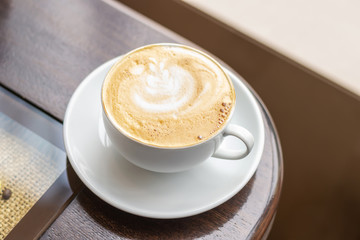 White Cup of Cappuccino with fine crema on wooden table in coffee shop