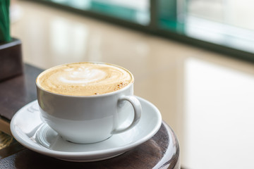 White Cup of Cappuccino with latte art. Coffee on wooden table next to cafe window