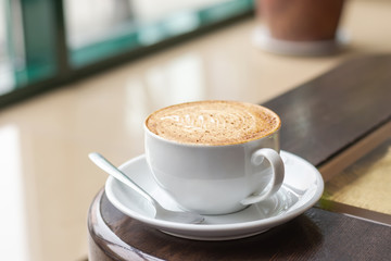 White Cup of Cappuccino with latte art. Coffee on wooden table next to cafe window
