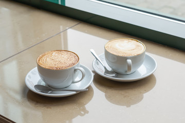 Two Cup of Cappuccino with beautiful crema. Latte art, selective focus. Coffee next to cafe window