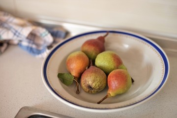 five pears in a plate with a blue border and a kitchen towel on the table