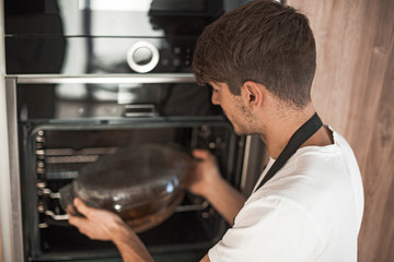 smiling young man warming up dinner in his kitchen