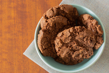 Chocolate flavoured cookies, with chocolate chips, in a green bowl on a tablecloth with a wooden background.